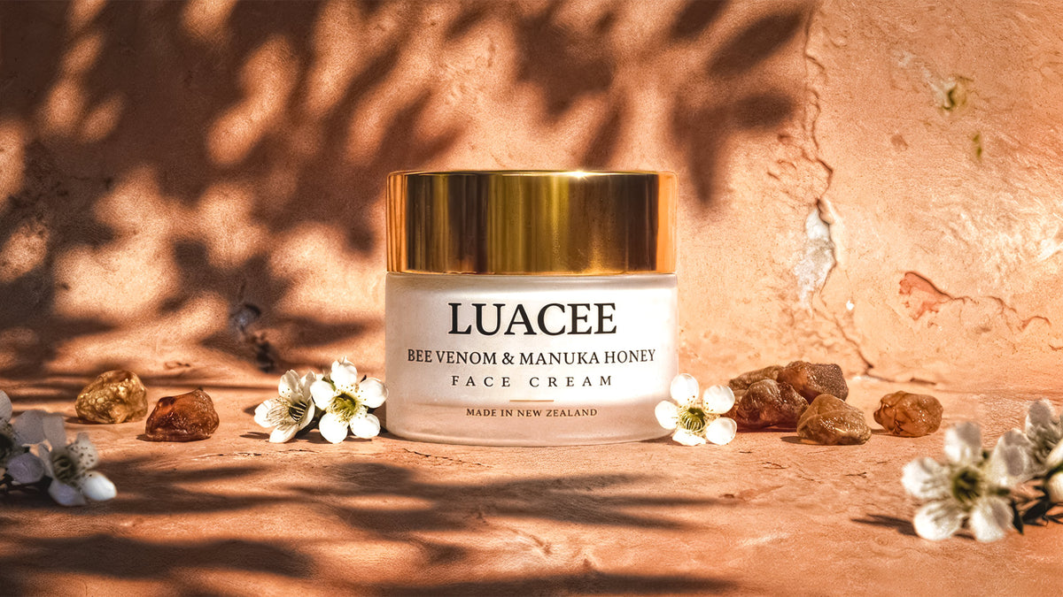 Luacee Bee Venom and Manuka Honey Face Cream jar on a warm peach surface under dappled leaf shadows with white blossom